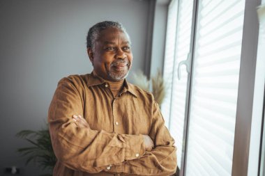 Ev Portresindeki Afrikalı Amerikalı kıdemli adam. Kameraya bakan gülümseyen son sınıf öğrencisi. Evde kendine güveni olan siyah bir adamın portresi. Gri bir arkaplanda duran yaşlı bir adamın portresi.