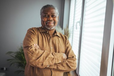 Ev Portresindeki Afrikalı Amerikalı kıdemli adam. Kameraya bakan gülümseyen son sınıf öğrencisi. Evde kendine güveni olan siyah bir adamın portresi. Gri bir arkaplanda duran yaşlı bir adamın portresi.