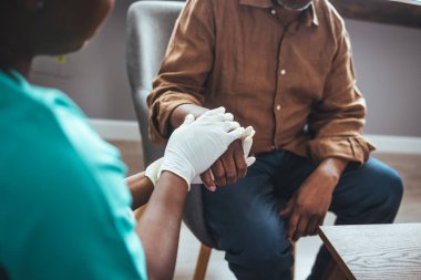 Huzurevinde yaşlı bir adamın elini tutan kadın sağlık çalışanı, ellerine odaklan. Kimliği belirlenemeyen genç bir doktorun kıdemli hastasının elini tutarken fotoğrafı.