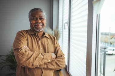 Ev Portresindeki Afrikalı Amerikalı kıdemli adam. Kameraya bakan gülümseyen son sınıf öğrencisi. Evde kendine güveni olan siyah bir adamın portresi. Gri bir arkaplanda duran yaşlı bir adamın portresi.