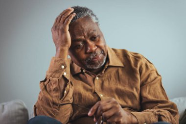 Başım ağrıyor. Migrenden muzdarip ve evde oturan yaşlı bir Afro-Amerikalı. Stresli yaşlı bir adam evde tek başına oturup kafasına dokunuyor. Sağlık hizmetleri, sağlık sorunları ve yaşlılık kavramı.