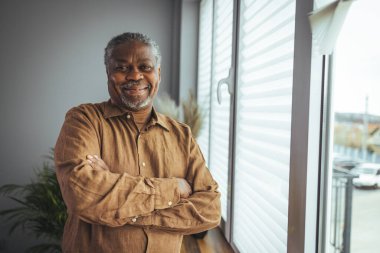 Ev Portresindeki Afrikalı Amerikalı kıdemli adam. Kameraya bakan gülümseyen son sınıf öğrencisi. Evde kendine güveni olan siyah bir adamın portresi. Gri bir arkaplanda duran yaşlı bir adamın portresi.