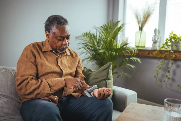 Active senior man measuring blood pressure with sphygmomanometer in bedroom. An older African American man measures blood pressure.