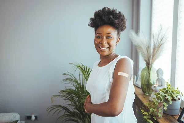 I got my covid-19 vaccine. Happy african american lady showing vaccinated arm after antiviral injection and smiling to camera, posing on blue studio background. Coronavirus vaccination