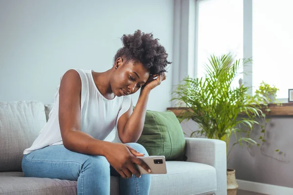 Frustrated young lady sitting on sofa, cuddling pillow, looking away at window. Lost in thoughts unhappy stressed millennial woman regretting of wrong decision, spending time alone in living room.