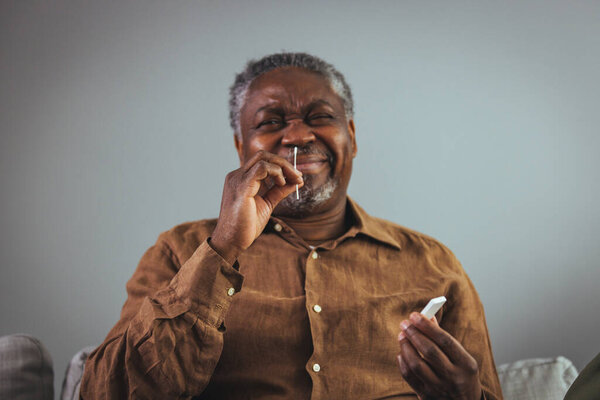 Senior African American man with gray hair and beard using the coronavirus (covid-19) antigen rapid self-test kit (atk) at home with a cotton nasal swab