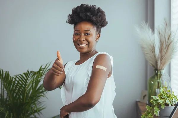 I got my covid-19 vaccine. Happy african american lady showing vaccinated arm after antiviral injection and smiling to camera, posing on blue studio background. Coronavirus vaccination