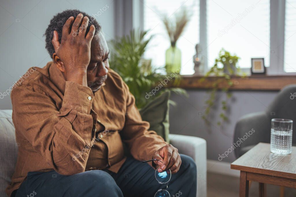 Thoughtful senior man sitting on couch. Depressed sad man sitting with hand on head thinking. Elderly man suffering from headache. Healthcare, pain, stress, age and people concept. 