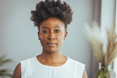 Mutlu kadın gülümsüyor ve kameraya bakıyor. Sıradan giyinmiş Afro-Amerikan kadın portresi ve evde gevşeyen kıvırcık kısa saç. Kopya alanı olan başarılı siyahi kadın portresi.