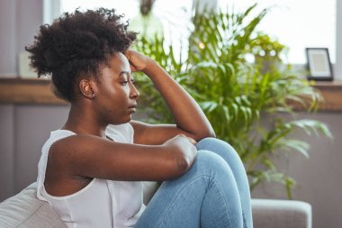 Genç ve çekici Afro-Amerikan kadın oturma odasındaki kanepede uzanıyor üzgün hissediyor yorgun ve endişeli zihinsel sağlık, sorunlar ve kırık kalp konsepti yüzünden depresyon geçiriyor..