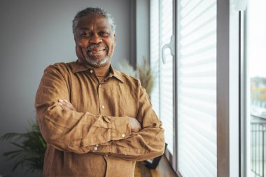 Gülümseyen yaşlı Afrikalı Amerikalı bir adamın portresi pencerenin yanında. Evdeki mutlu yaşlı adamın portresi. Mutlu Afrikalı Amerikalı adam gülümsüyor.
