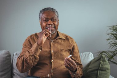 60 'lı yaşlarda bir adam evde Covid-19 yanal akış testi yaptırıyor. Adam Afro-Amerikan kökenli ve bir gömlek giyiyor. Kopyalama alanı.