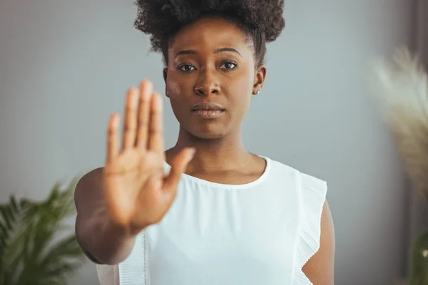 Photo of African american young woman making stop gesture with palm of her hand on grey background. Serious african american woman protesting against bullying.