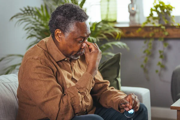 A headache. An elderly African-American who suffers from migraines and sits at home. Stressful older man sitting in bed at home alone, touching his head. Health care, health problems in old age concept.
