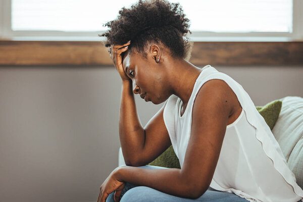 Расстроенная женщина, разочарованная работой или отношениями, сидящая на диване, обнимающая колени, закрытая лицом в руке, чувствующая отчаяние и тревогу, одиночество, имеющая психологические проблемы
