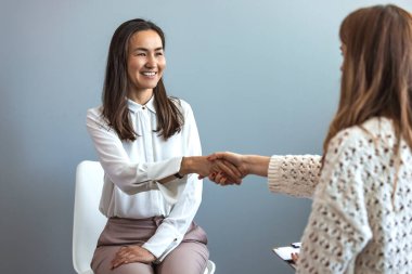 Hoş insanlar birbirini selamlıyor. Etkili terapi. Neşeli kadın hasta ve psikolog ofiste el sıkışıyor. Başarılı bir tedaviden sonra Asyalı kadın psikoterapistine minnettar.