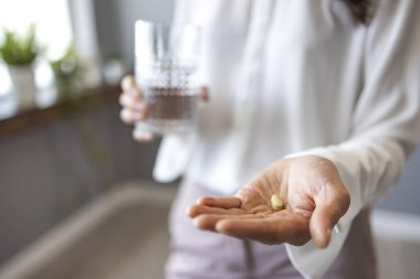 Bir bardak su ve beyaz hap tutan kadın elleri. Vitaminler alınıyor. Tıbbi, eczane ve sağlık hizmetleri konsepti. Elinde haplar ve bir bardak su olan bir kadın.. 