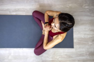 Mutlu bir Asyalı kadın evinde bir kanepeye oturur ve bilge elleriyle nilüfer çiçeği pozisyonunda meditasyon yapar. Gülümseyen genç Asyalı kadın oturma odasındaki kanepede dinleniyor, yoga yapıyor, negatif duyguları serbest bırakıyor.