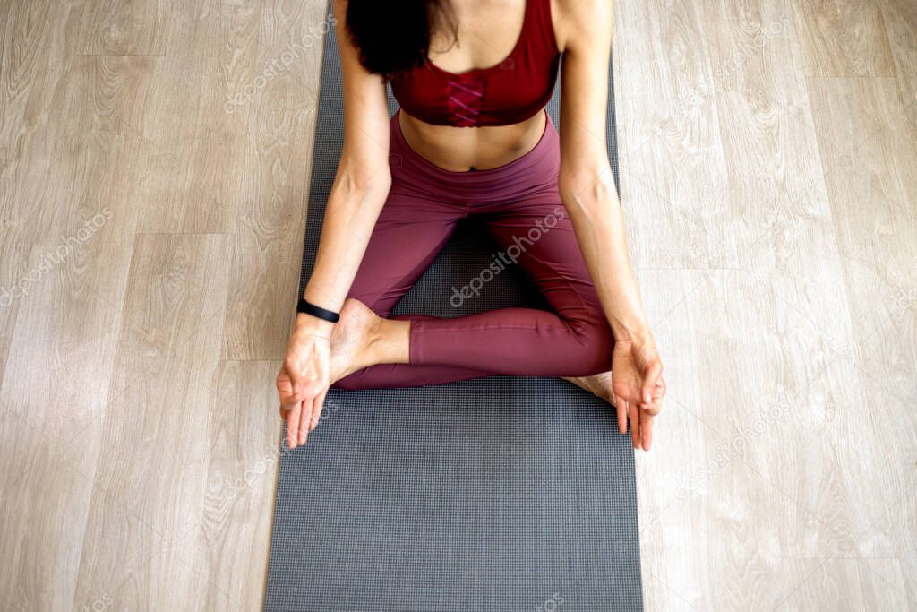 A slender Asian yoga girl in sportswear is sitting in a Lotus pose up close. A calm girl is sitting in her living room. Practicing yoga at home on a mat. No stress, no freedom, no concept of meditation.