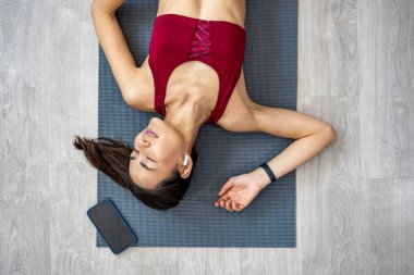 Attractive Asian woman practices the concept of yoga, sits in an exercise on a yoga mat, Balasana pose, exercises, wears sportswear, sleeveless T-shirt and pants, full length, white attic background.  clipart