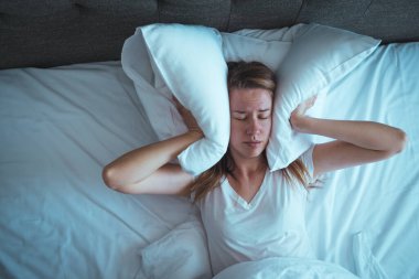 Yatakta yatan güzel beyaz kadın baş ağrısı / uykusuzluk / migren / stres yaşıyor. Yüzünü ellerle örten genç bir kadın. Uykusuzluk çeken umutsuz kız uyumaya çalışıyor.