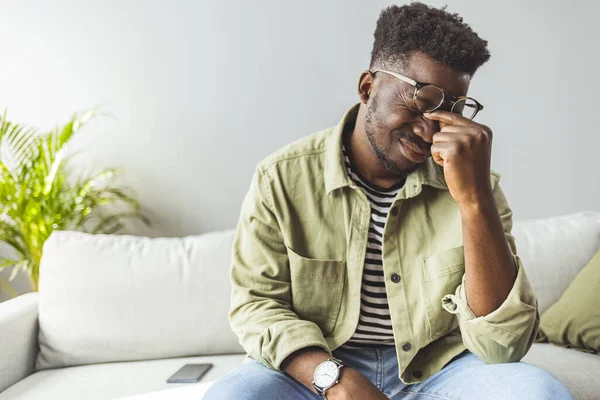 Genç Afrikalı adam elleriyle kafasına dokunuyor ve evdeki kanepede otururken gözlerini kapalı tutuyor. Zenci adam stresli ve baş ağrısı çekiyor. Hasta ve yorgun hissediyorum.. 