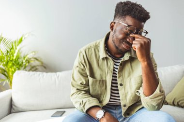 Genç Afrikalı adam elleriyle kafasına dokunuyor ve evdeki kanepede otururken gözlerini kapalı tutuyor. Zenci adam stresli ve baş ağrısı çekiyor. Hasta ve yorgun hissediyorum.. 