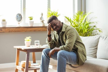 Üzgün Afro-Amerikalı bir adam elleriyle başını sıkıyor, acı içinde kıvranıyor, evde baş ağrısı çekiyor, kopyalama uzayı. Zenci adam stresli ve baş ağrısı çekiyor.