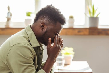 Hayal kırıklığına uğramış orta yaşlı bir adam. Elleri başının üstünde, evdeki kanepede oturuyor. Korkunç migreni, aşırı yükü ve aşırı çalışma konsepti olan endişeli Afrikalı Amerikalı iş adamı.