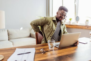 Male businessman who suffers back pain from working from home. Shot of a young businessman suffering from backache while working at his desk during a day at work