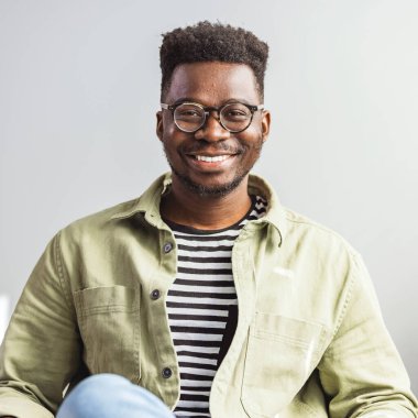 Gözlüklü, gülümseyen adam kameraya bakıyor. Evde kendine güveni olan siyah bir adamın portresi. Başarılı girişimci kendini tatmin olmuş hissediyor. Gülümseyen Afro-Amerikan milenyum işadamı gözlüklü