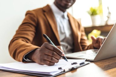 Odaklanmış Afrikalı genç iş adamı internetten bilgisayardan webinar podcast izliyor eğitim konferansını dinliyor notlar alıyor çalışma masasına oturuyor ve konsept öğreniyor.