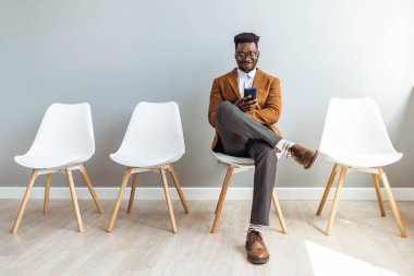 Studio shot of a young man waiting against a gray background. Young businessman waiting for job interview. Portrait of a businessman sitting on a chair