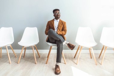 Male entrepreneur waiting for job interview in a hallway. He's the last one left to be interviewed. Full length studio shot of a handsome young businessman sitting against a gray background