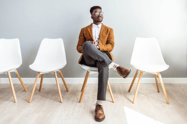 Studio shot of a young man waiting against a gray background. Young businessman waiting for job interview. Portrait of a businessman sitting on a chair