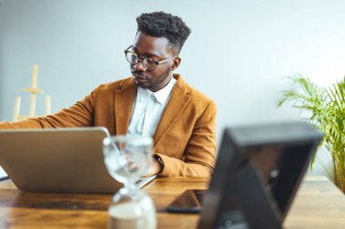 Afro-Amerikan iş adamı ofiste dizüstü bilgisayarla çalışıyor.