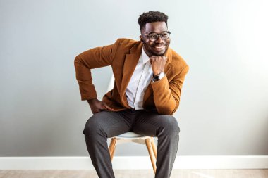 young african-american man sitting on chair with hand on chin against grey wall background