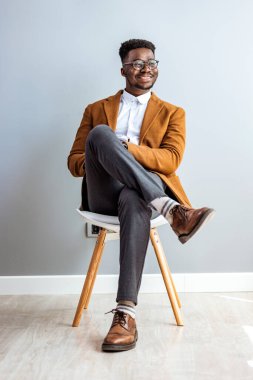 smiling african-american businessman sitting on chair and looking away in studio