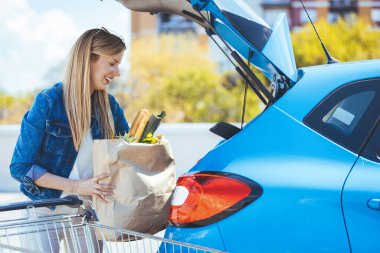 Genç bir kadın alışveriş malzemelerini arabaya yüklüyor.