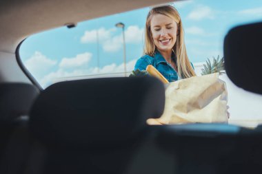 Sokakta alışveriş torbası taşıyan genç bir kadın. Arabanın ön camından görüntüle