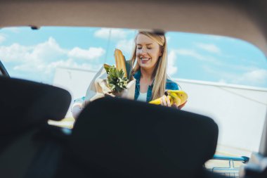 Sokakta alışveriş torbası taşıyan genç bir kadın. Arabanın ön camından görüntüle