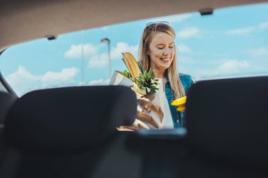 Sokakta alışveriş torbası taşıyan genç bir kadın. Arabanın ön camından görüntüle