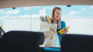 Sokakta alışveriş torbası taşıyan genç bir kadın. Arabanın ön camından görüntüle