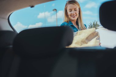 Sokakta alışveriş torbası taşıyan genç bir kadın. Arabanın ön camından görüntüle