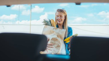 Sokakta alışveriş torbası taşıyan genç bir kadın. Arabanın ön camından görüntüle