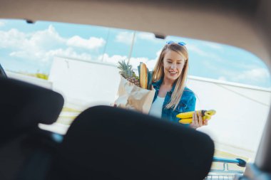 Sokakta alışveriş torbası taşıyan genç bir kadın. Arabanın ön camından görüntüle