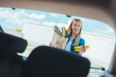 Sokakta alışveriş torbası taşıyan genç bir kadın. Arabanın ön camından görüntüle