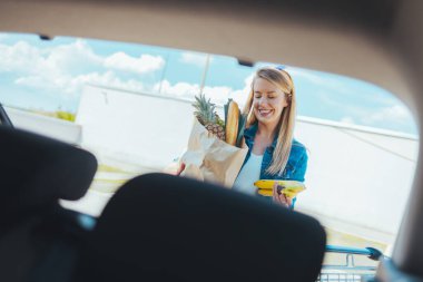Sokakta alışveriş torbası taşıyan genç bir kadın. Arabanın ön camından görüntüle