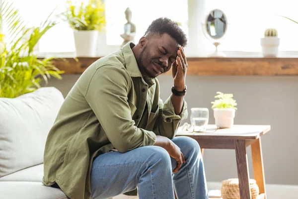 Evdeki kanepede otururken stresli görünen bir adamın fotoğrafı. Zor bir günün ardından baş ağrısı çeken genç Afro-Amerikalı iş adamı, evdeki kanepede oturup, uzayı kopyalıyor.