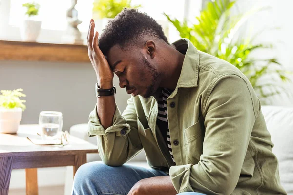 Hayal kırıklığına uğramış orta yaşlı bir adam. Elleri başının üstünde, evdeki kanepede oturuyor. Korkunç migreni, aşırı yükü ve aşırı çalışma konsepti olan endişeli Afrikalı Amerikalı iş adamı.